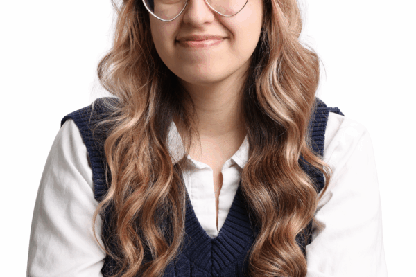 Headshot of Jessica. She has long pink and brown hair, is wearing heart shaped glasses, and a navy sweater vest with a white collared shirt underneath.