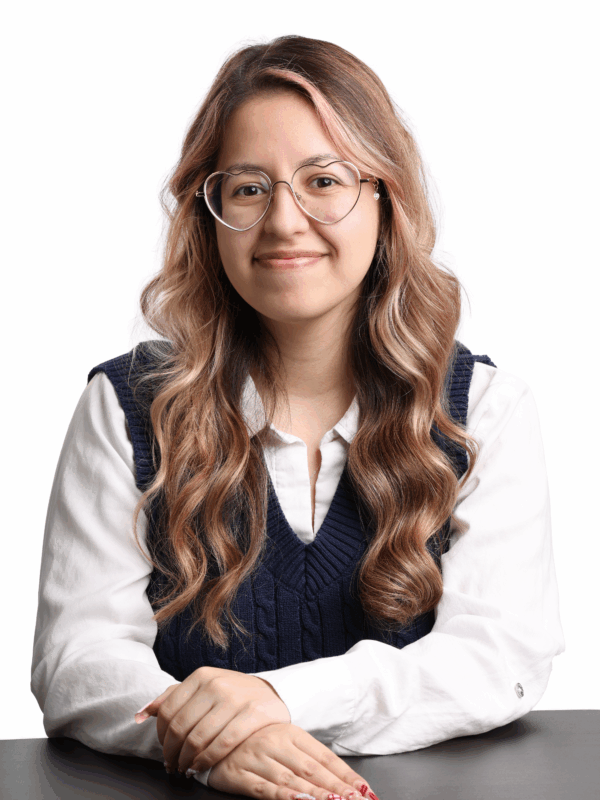 Headshot of Jessica. She has long pink and brown hair, is wearing heart shaped glasses, and a navy sweater vest with a white collared shirt underneath.