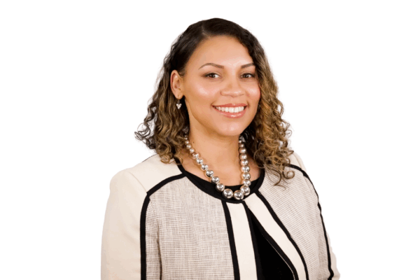 Woman with shoulder-length curly hair, wearing a cream and black jacket with a pearl necklace, smiling in front of a white background.