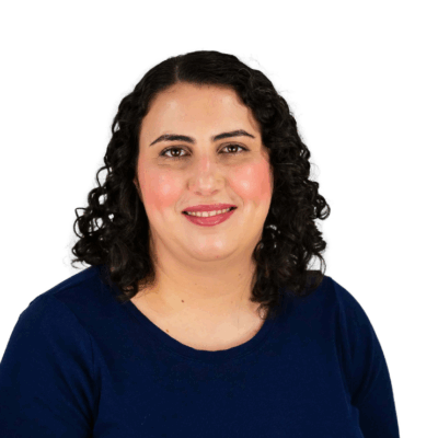 Woman with shoulder-length dark curly hair, wearing a navy blue top, smiling gently in front of a white background.