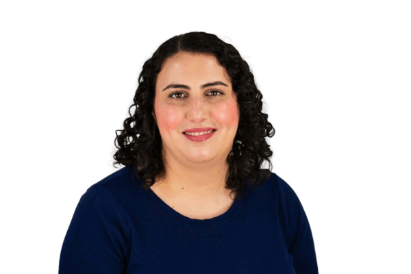 Woman with shoulder-length dark curly hair, wearing a navy blue top, smiling gently in front of a white background.