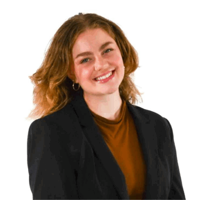 Woman with shoulder-length wavy hair, wearing hoop earrings, a rust-colored top, and a black blazer, smiling in front of a white background.