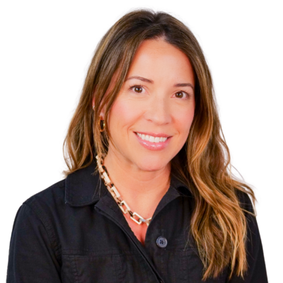 Woman with long wavy hair, wearing a black zip-up jacket and a chunky chain necklace, smiling against a white background.