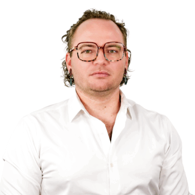 Man with wavy hair and tortoiseshell glasses, wearing a white button-down shirt, facing forward with a neutral expression.