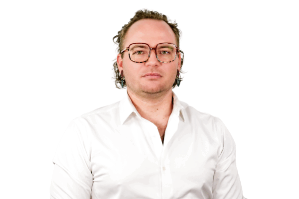 Man with wavy hair and tortoiseshell glasses, wearing a white button-down shirt, facing forward with a neutral expression.