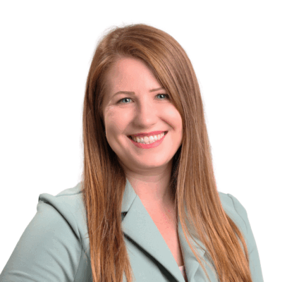 Woman with long straight red-blonde hair, wearing a light green blazer, smiling confidently in front of a white background.