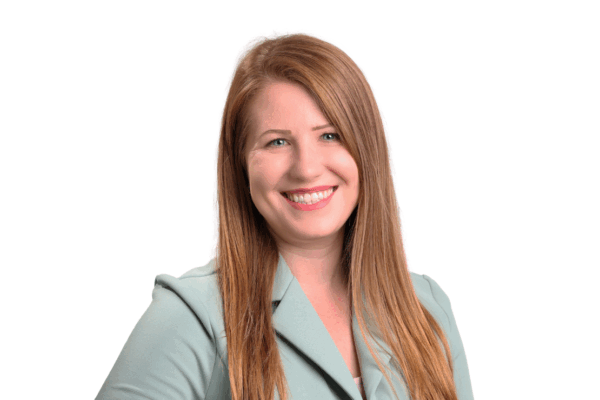 Woman with long straight red-blonde hair, wearing a light green blazer, smiling confidently in front of a white background.