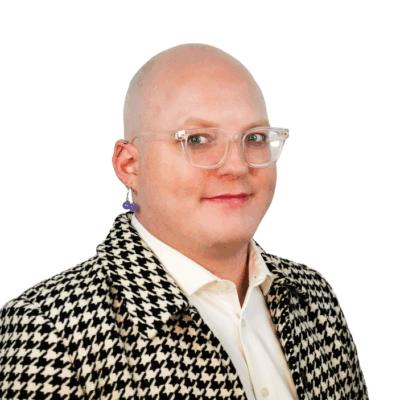 Bald person with clear glasses and a bold earring, wearing a black and white houndstooth jacket over a white shirt, smiling slightly.