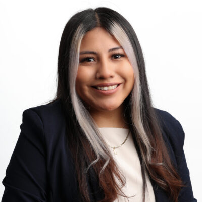 Headshot of Lin. She is a tan woman with black hair and two silver strands of hair framing her face. She is wearing a white top and a navy blazer.