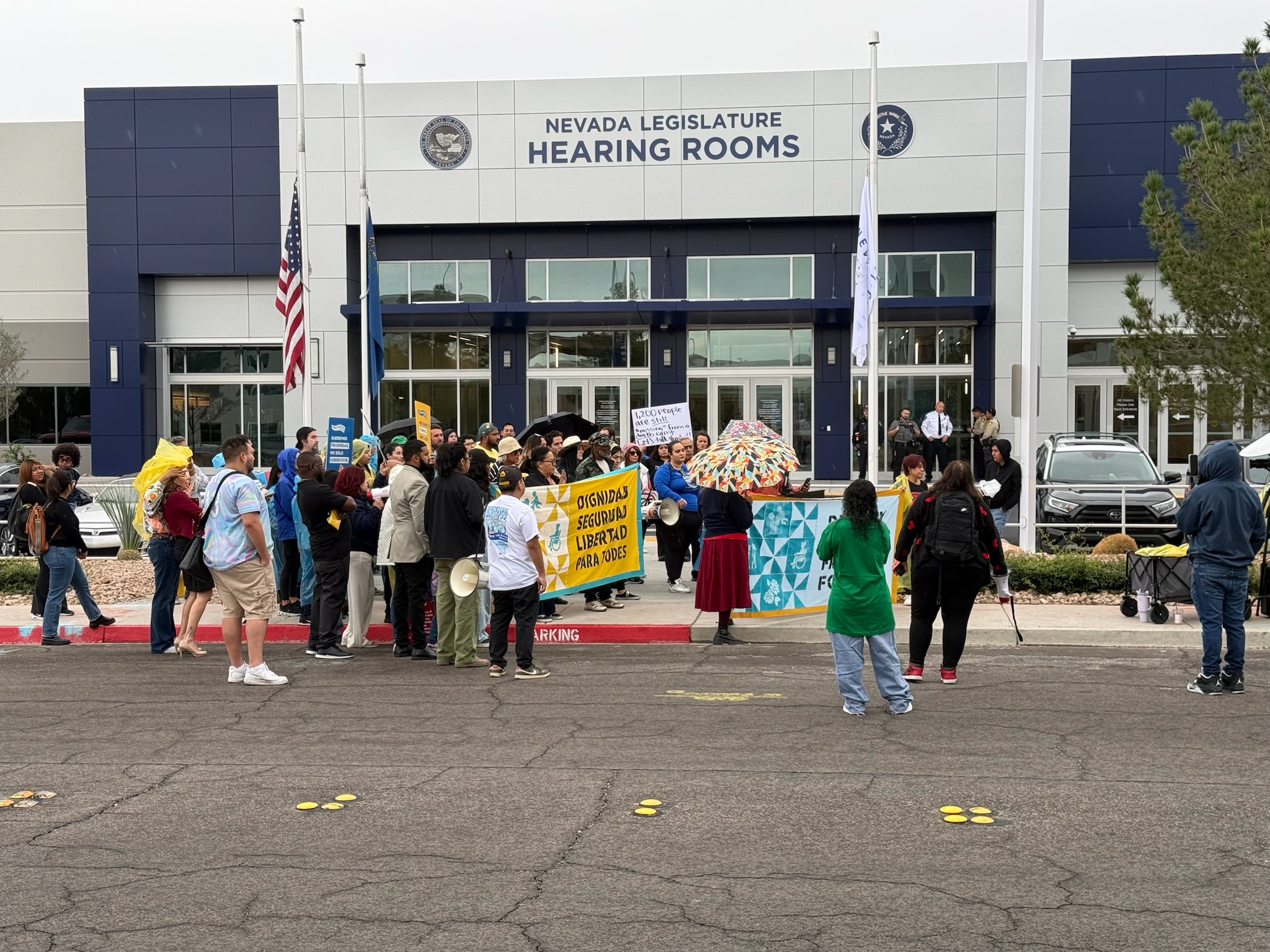 Group of people standing in front of Nevada Legislature Hearing Rooms with banners and signs.