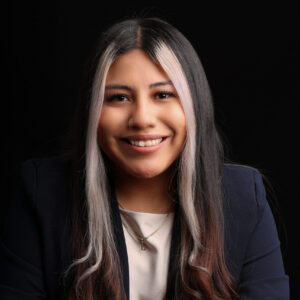 Headshot of Lin. She is a tan woman with black hair and two silver strands of hair framing her face. She is wearing a white top and a navy blazer.