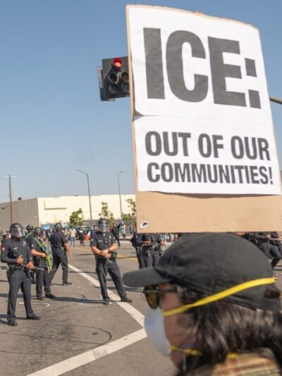 ICE officers in the street and a protest sign being held up that reads "ICE out of our communities."
