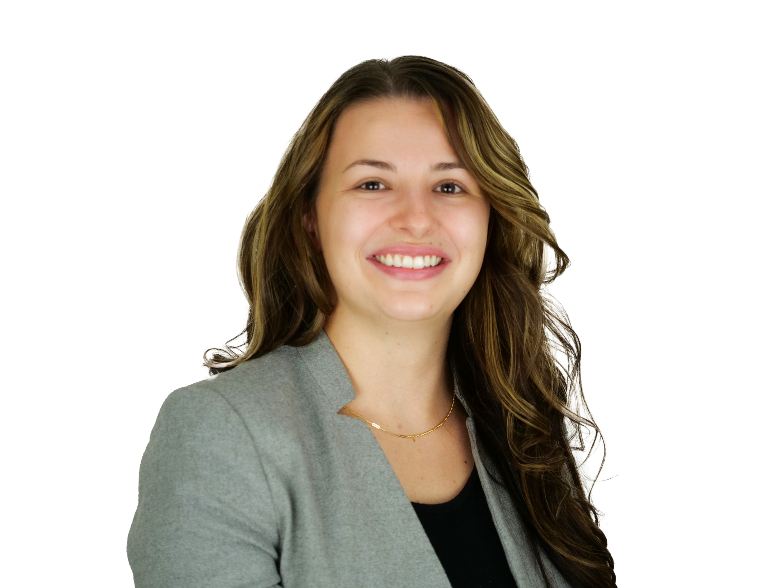 Woman with long curled brown hair, wearing a black top and grey blazer, smiling in front of a white background.