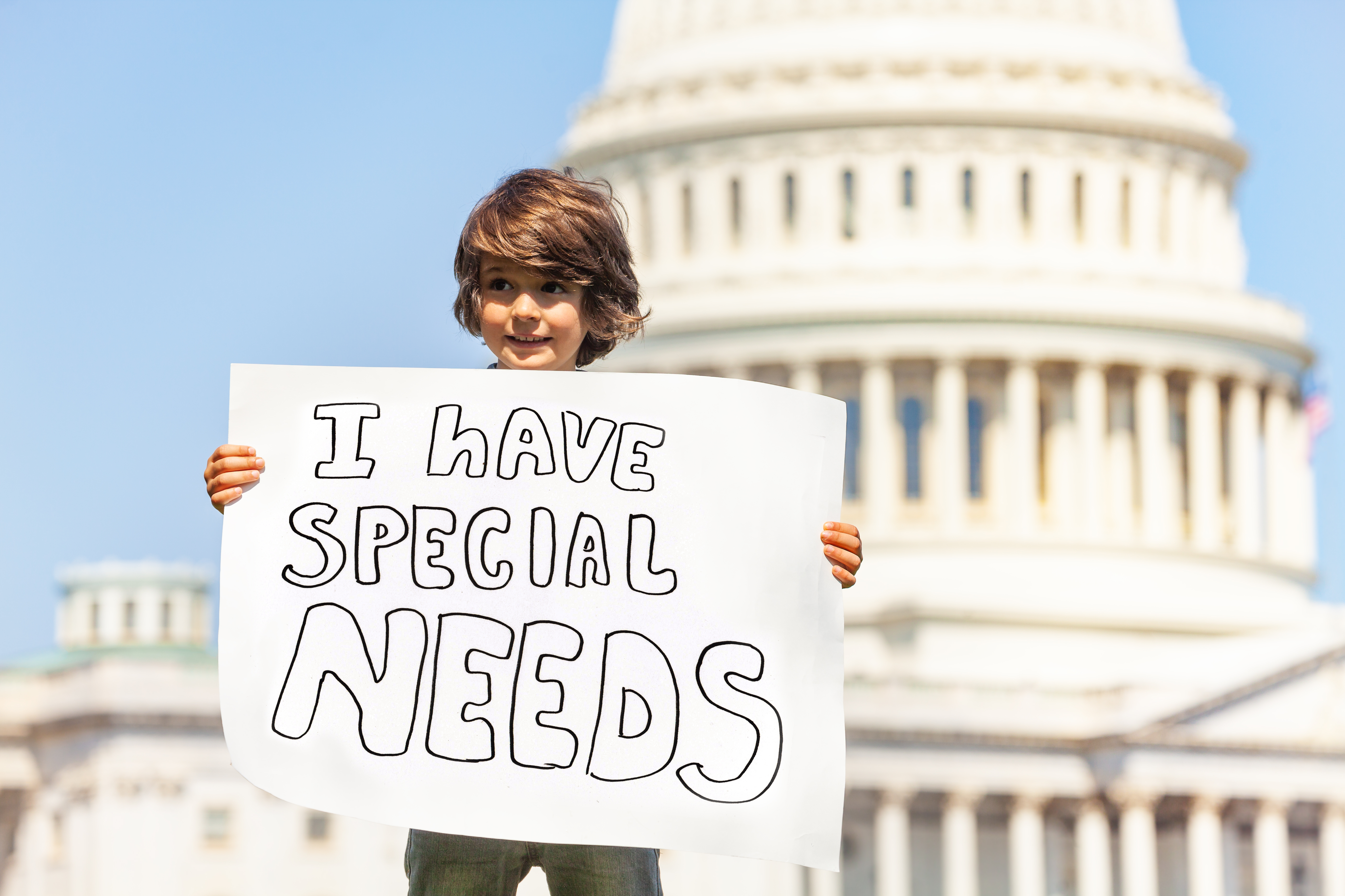 A little boy in front of the Capitol building. He is holding a sign that says "I have special needs."