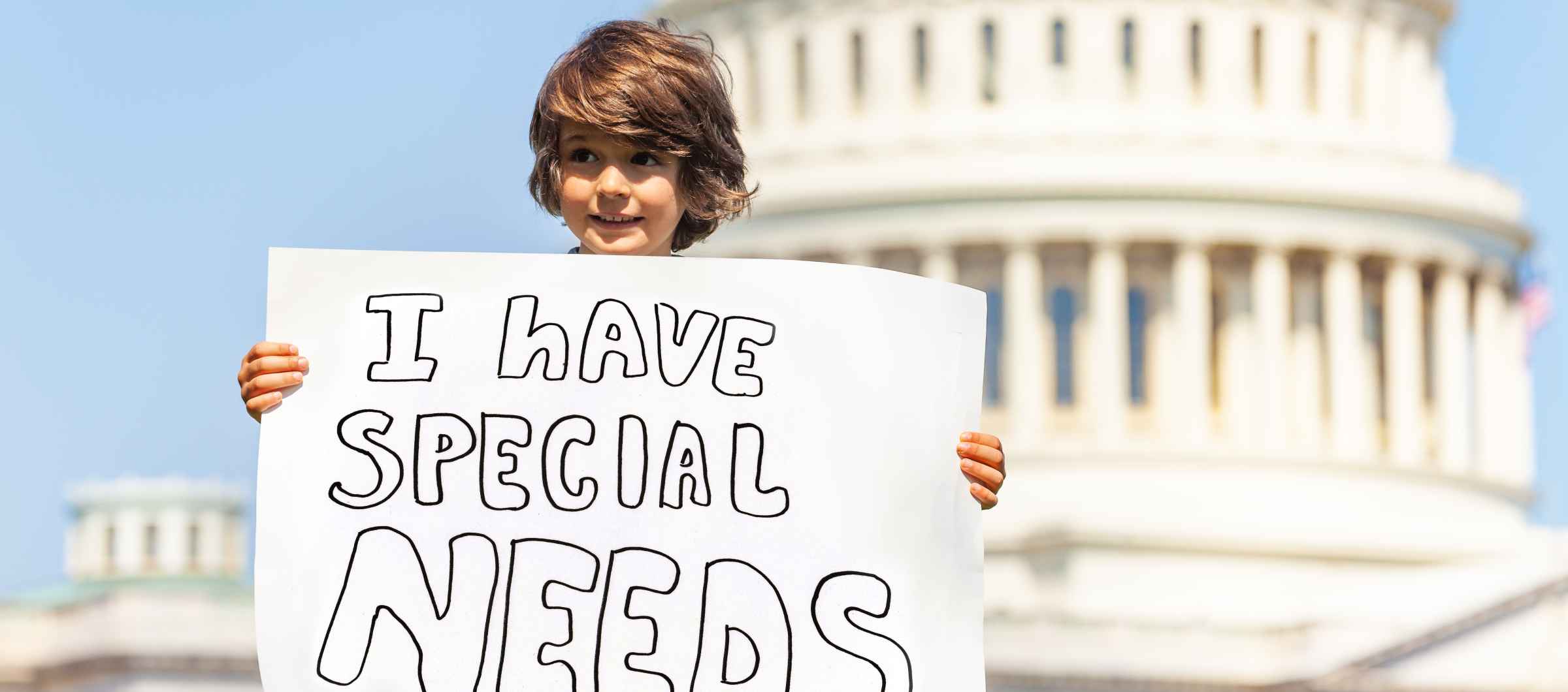 Little boy in front of the Capitol building holding a sign that says "I have special needs."
