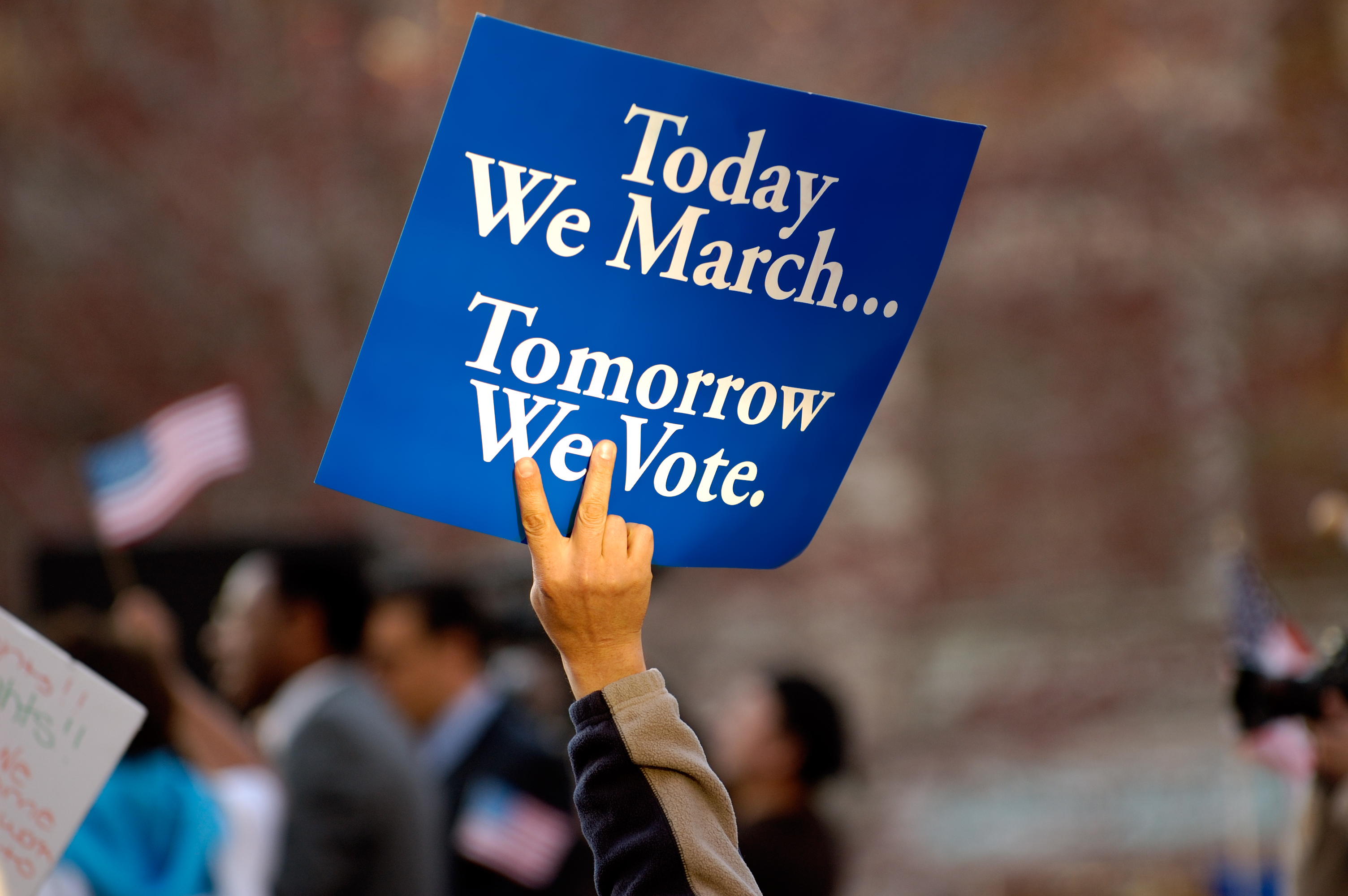 A blue sign with white text on it. It says "Today we march, tomorrow we vote."