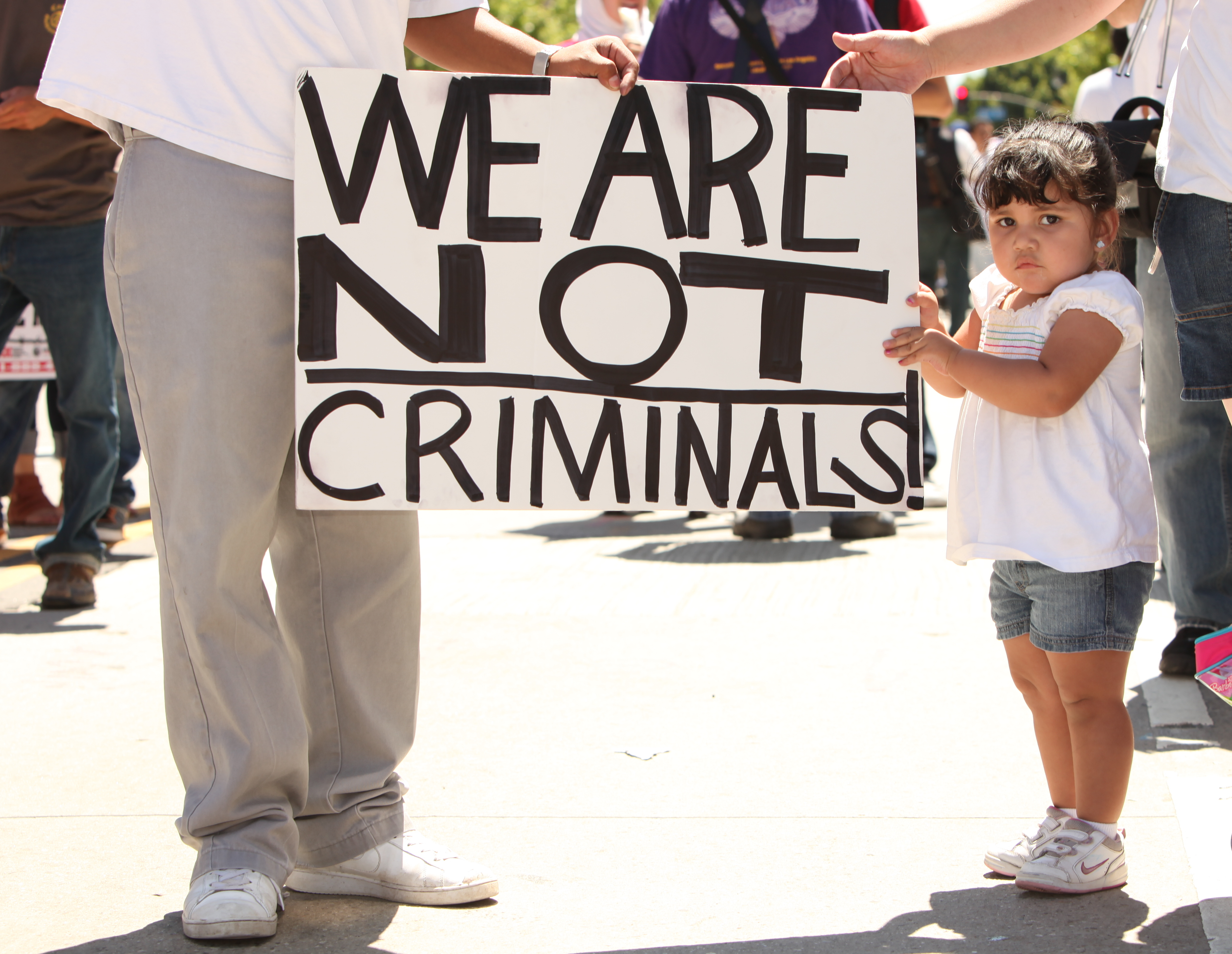 Child holding sign that reads "We are not criminals."