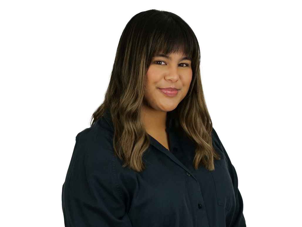 Jordyn in front of white background. She is wearing a navy blue long sleeved collared shirt.