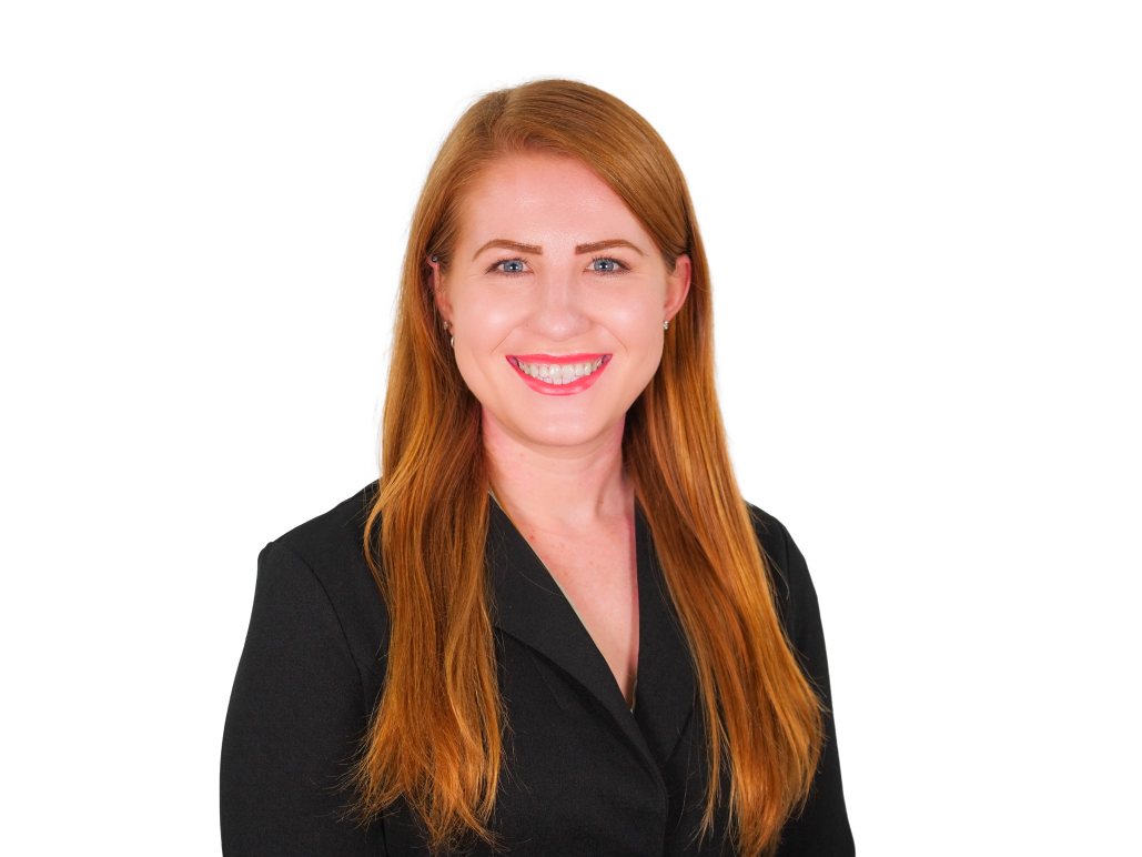 Tia in front of a white background. She is wearing a black button up. She is a white woman with red hair and blue eyes.