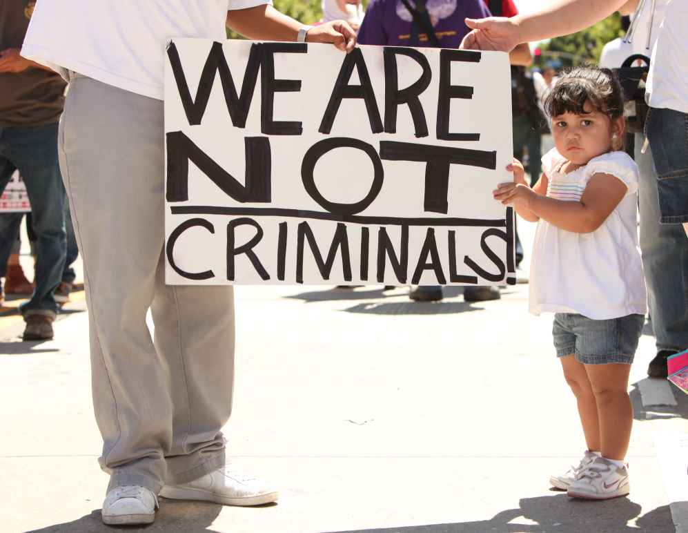 Child holding sign that reads "We are not criminals."