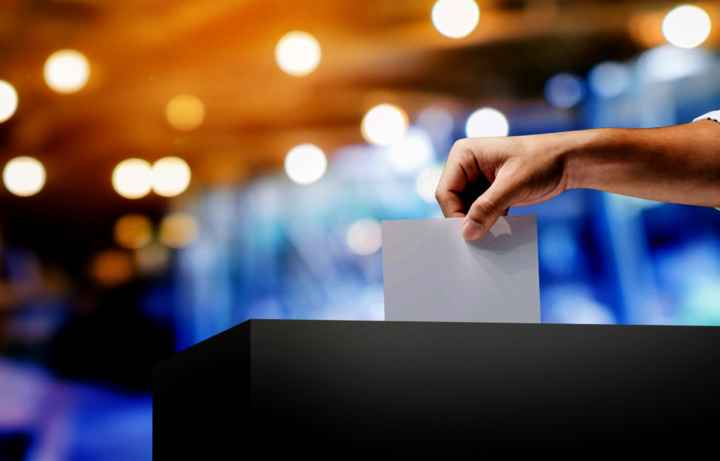 a photo a hand putting a blank paper into a ballot box. the background is blurred.