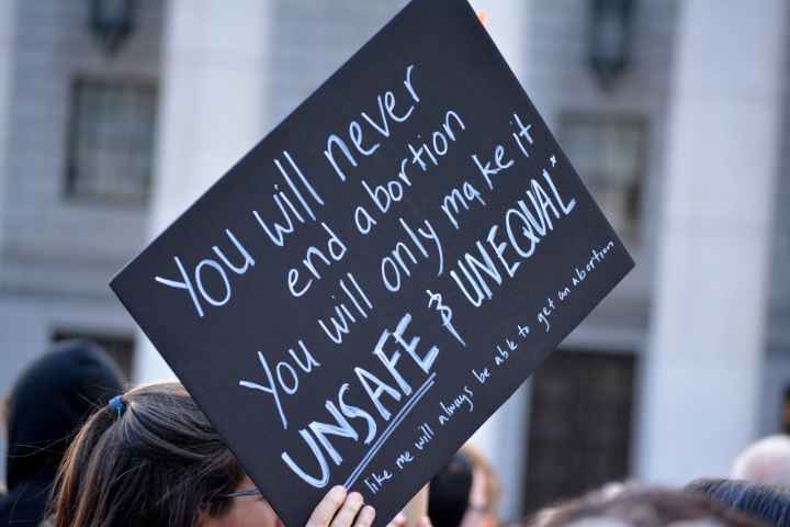 A black protest sign with white text that says "You will never end abortion. You will only make it UNSAFE & UNEQUAL"