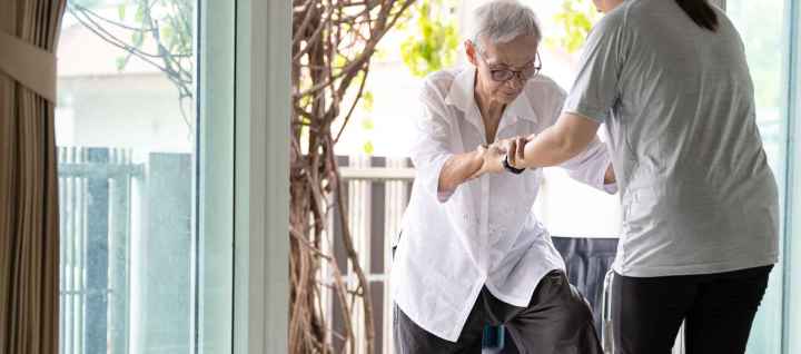 Woman helping elderly woman into house through sliding glass door.