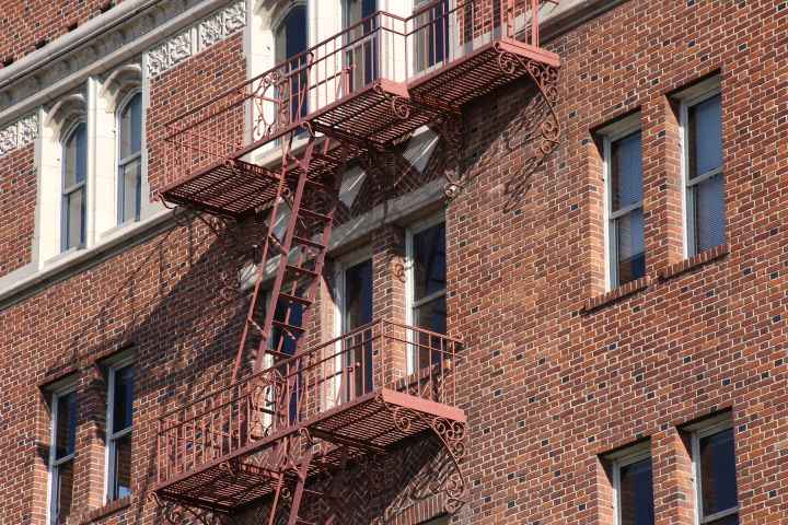 Side of apartment building made out of brick wall with fire escape going down the side. 