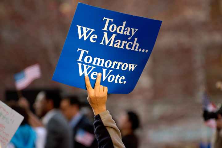 A blue sign with white text on it. It says "Today we march, tomorrow we vote."