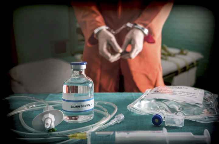 prisoner in orange jump suit and handcuffs standing behind execution table