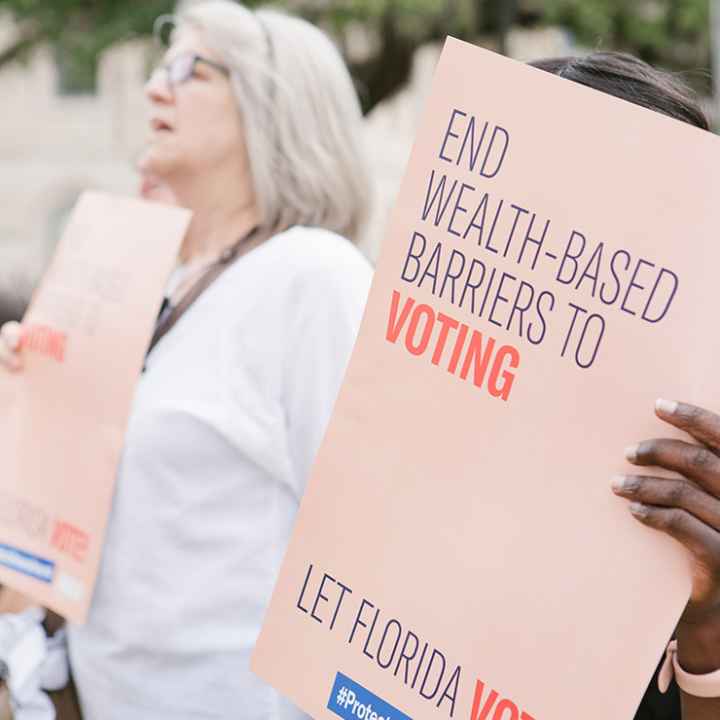 Woman holding sign reading 'End wealth based barriers to voting"