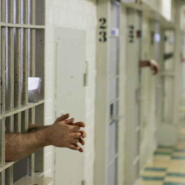 Prisoners reach through the metal bars of their cells.