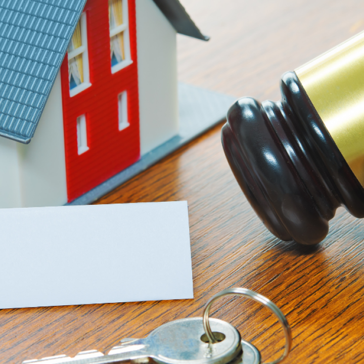 left to right: a small toy house, a deed, two keys, and a gavel sitting on a wooden surface