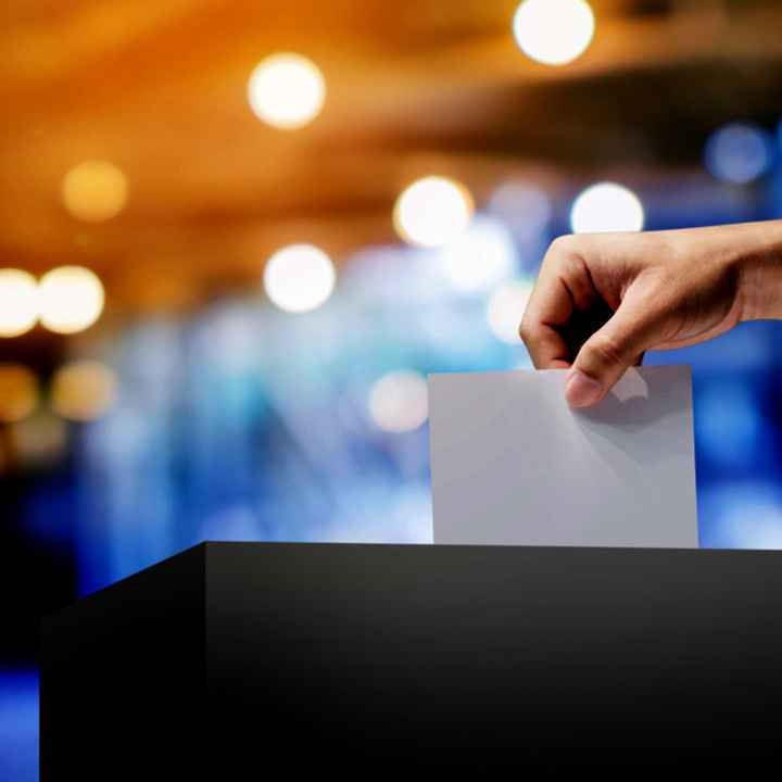 a photo a hand putting a blank paper into a ballot box. the background is blurred.