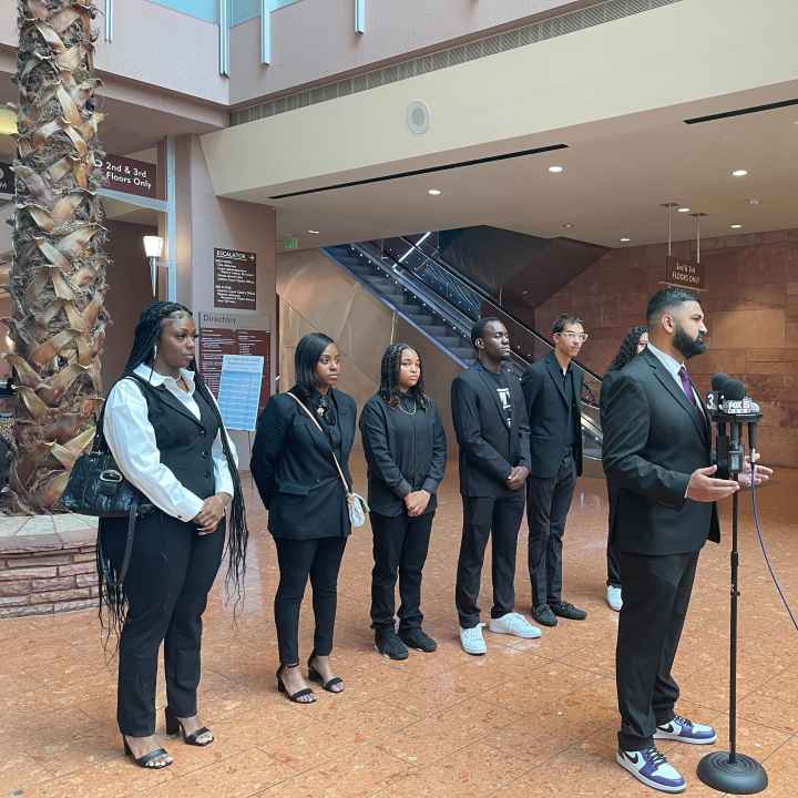 Athar Haseebullah standing at a microphone speaking to the press while the 6 Emerging Leaders Board Members stand behind him in a line.