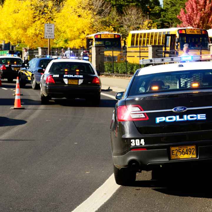 Line of police cars parked in front of school. There is also a line of school buses.