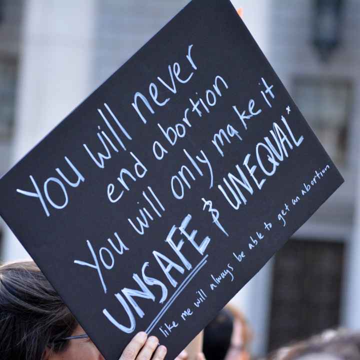 A black protest sign with white text that says "You will never end abortion. You will only make it UNSAFE & UNEQUAL"