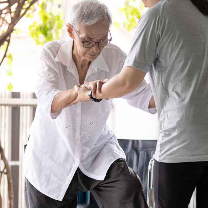 Woman helping elderly woman into house through sliding glass door.