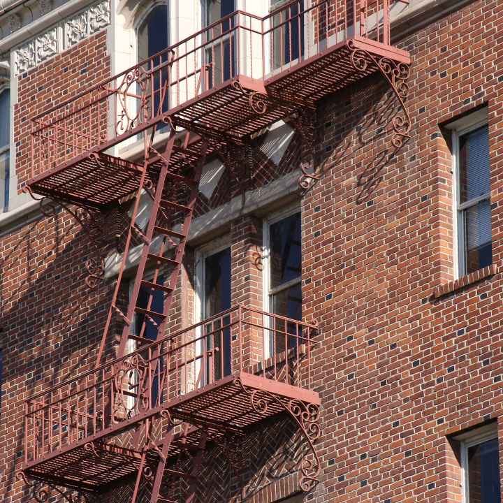 Side of apartment building made out of brick wall with fire escape going down the side. 