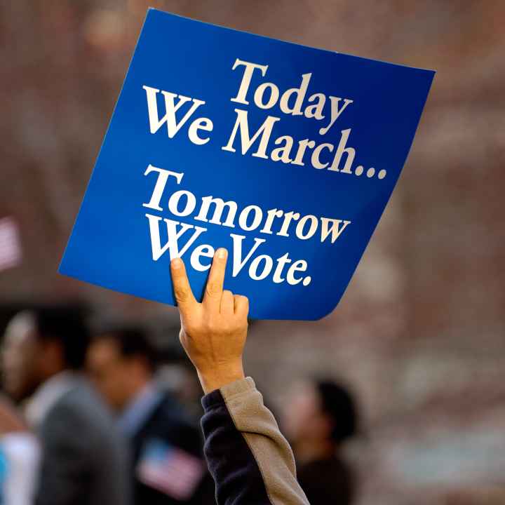 A blue sign with white text on it. It says "Today we march, tomorrow we vote."