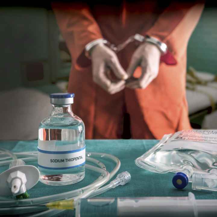 prisoner in orange jump suit and handcuffs standing behind execution table